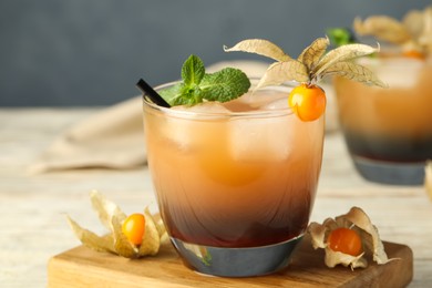 Photo of Refreshing cocktail decorated with physalis fruit on wooden table against grey background