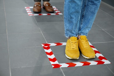 Photo of People standing on taped floor markings for social distance, closeup. Coronavirus pandemic