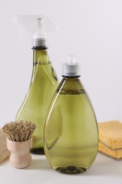 Bottles of cleaning product, brush and sponges on white background