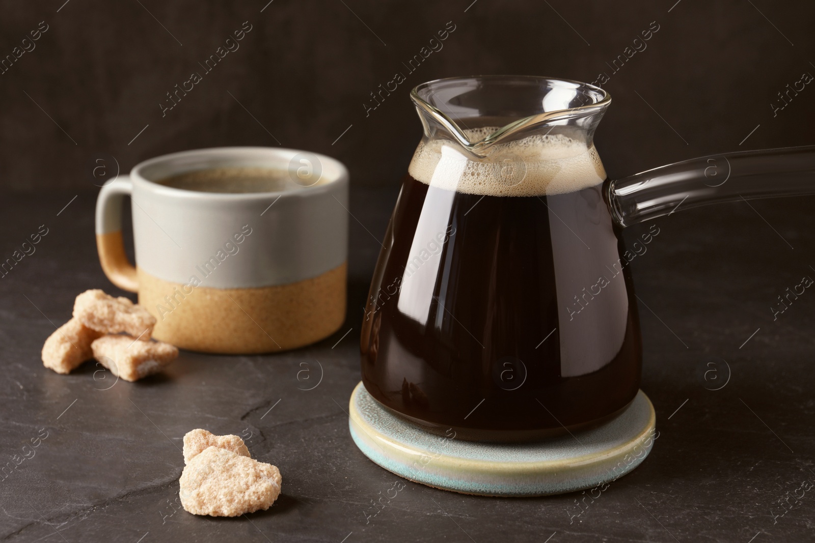 Photo of Turkish coffee in glass cezve and cup on dark grey table