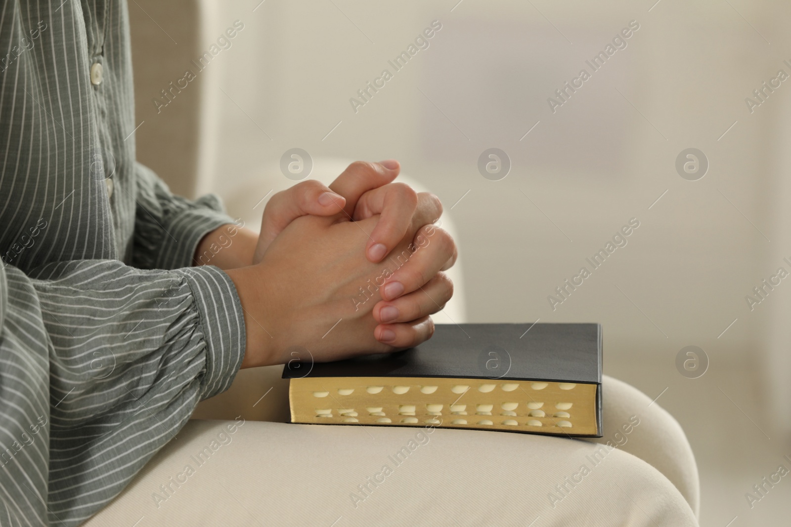 Photo of Religious woman praying over Bible indoors, closeup