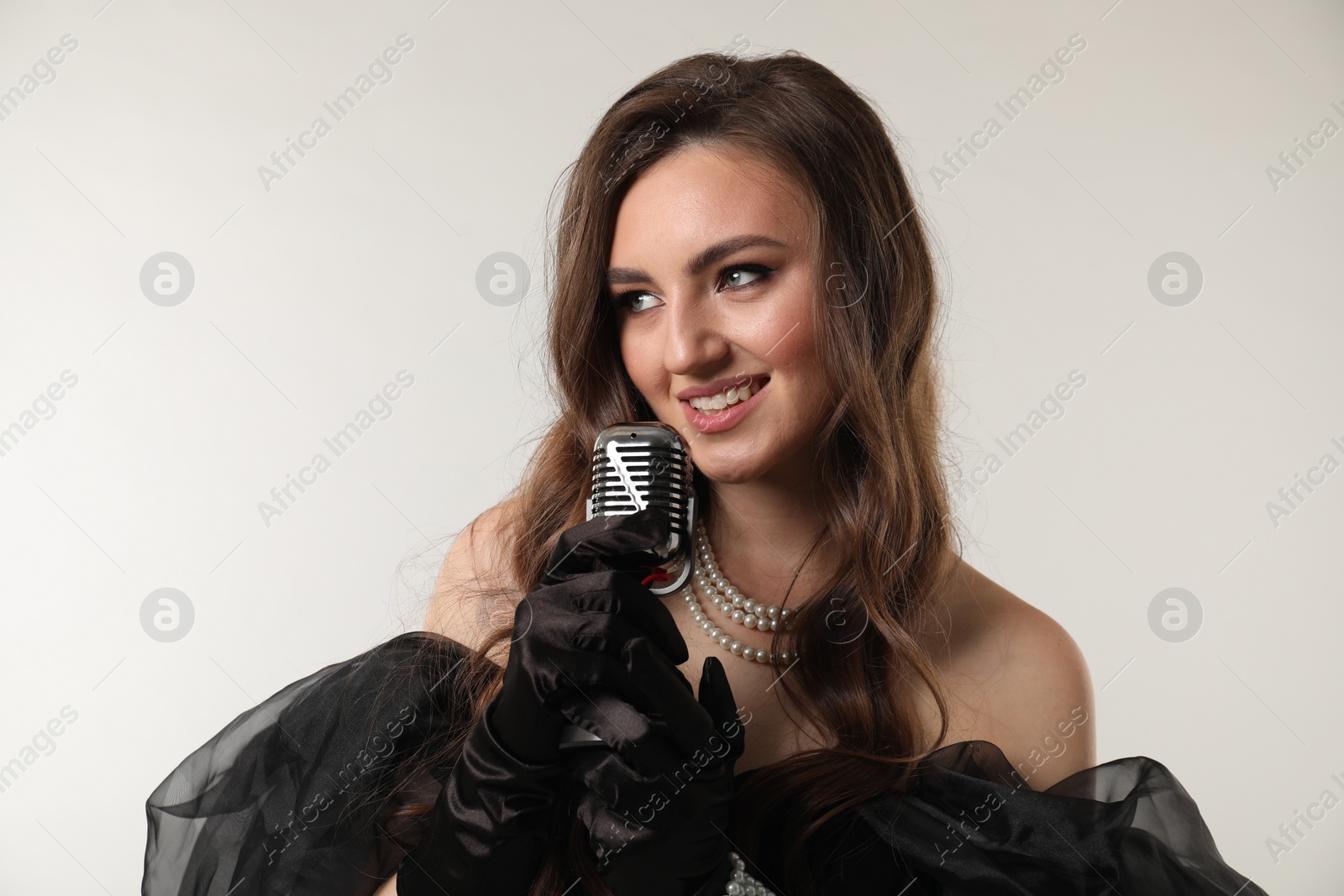 Photo of Beautiful young woman with microphone singing on light grey background