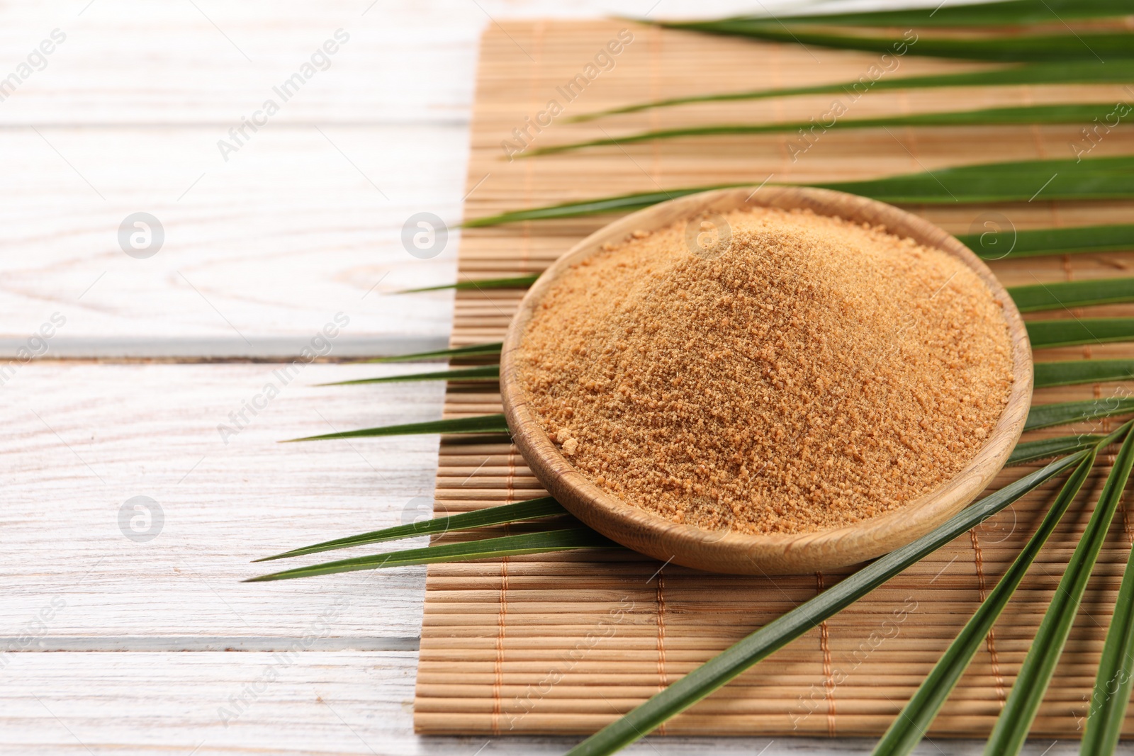 Photo of Coconut sugar, palm leaves and bamboo mat on wooden rustic table, closeup. Space for text