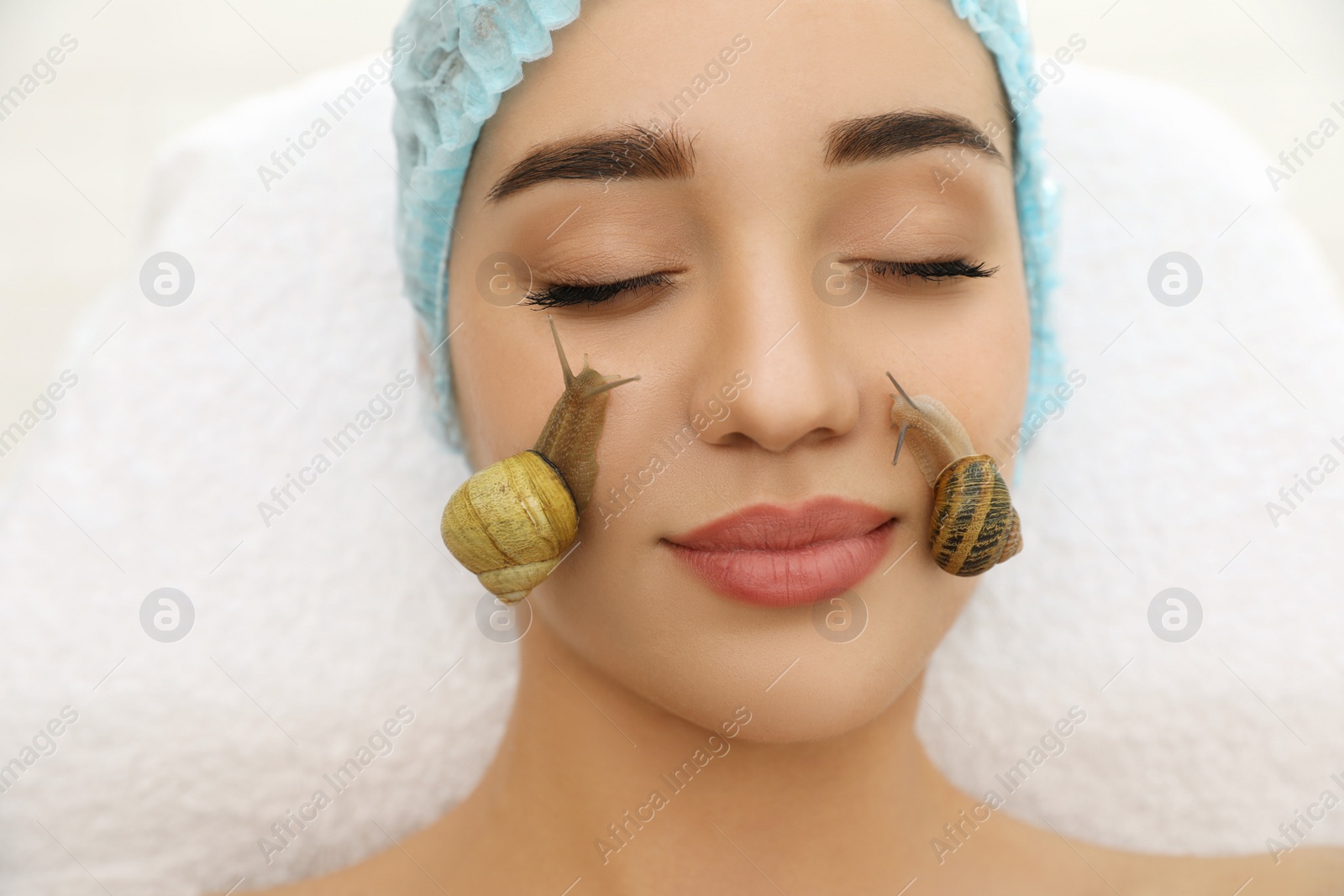 Photo of Young woman receiving snail facial massage in spa salon, closeup