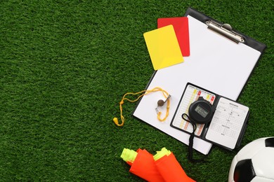 Soccer ball and different referee equipment on green grass, flat lay. Space for text