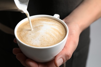 Woman pouring milk into cup of coffee on grey background, closeup