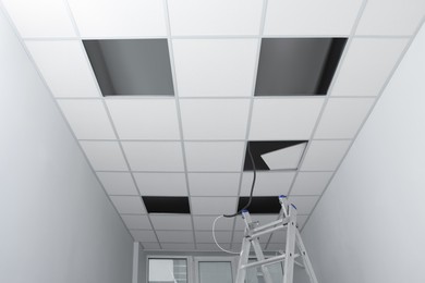Photo of Low angle view on PVC tiles. Installing ceiling lighting