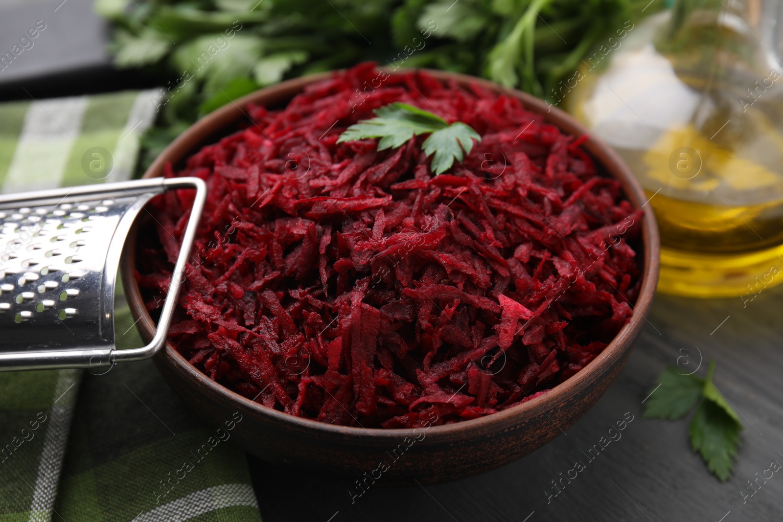 Photo of Grated red beet with parsley in bowl and grater on table, closeup