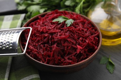 Photo of Grated red beet with parsley in bowl and grater on table, closeup
