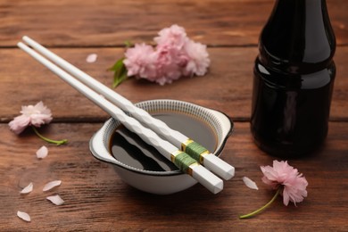 Photo of Bottle, bowl with soy sauce, chopsticks and flowers on wooden table