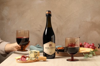 Photo of Woman holding glass of red wine at table with different snacks, closeup