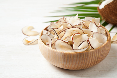 Tasty coconut chips on white wooden table