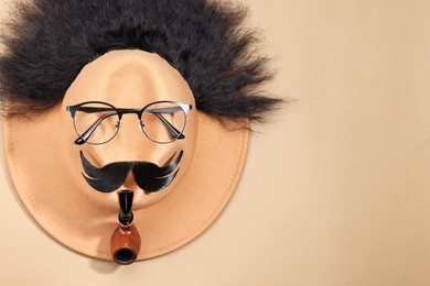 Man's face made of artificial hair, mustache, glasses and hat on beige background, top view. Space for text