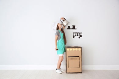 Photo of Little child in chef hat playing with carton stove indoors