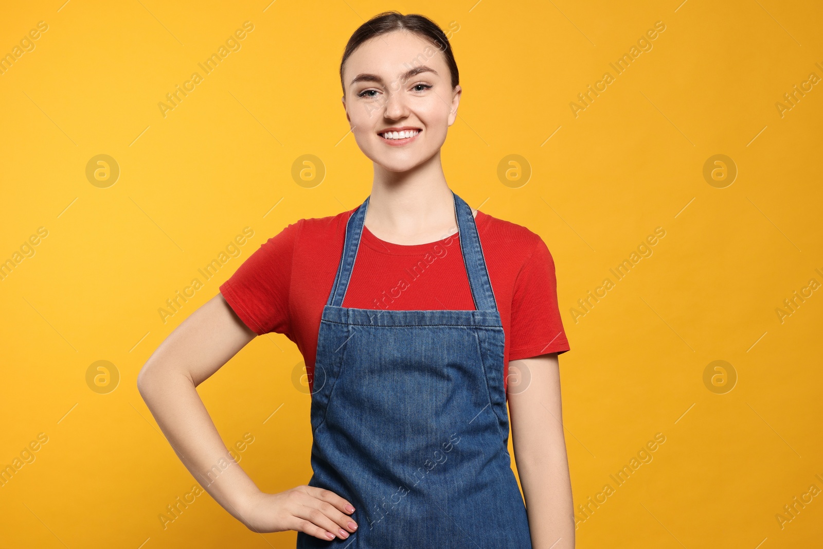 Photo of Beautiful young woman in clean denim apron on orange background