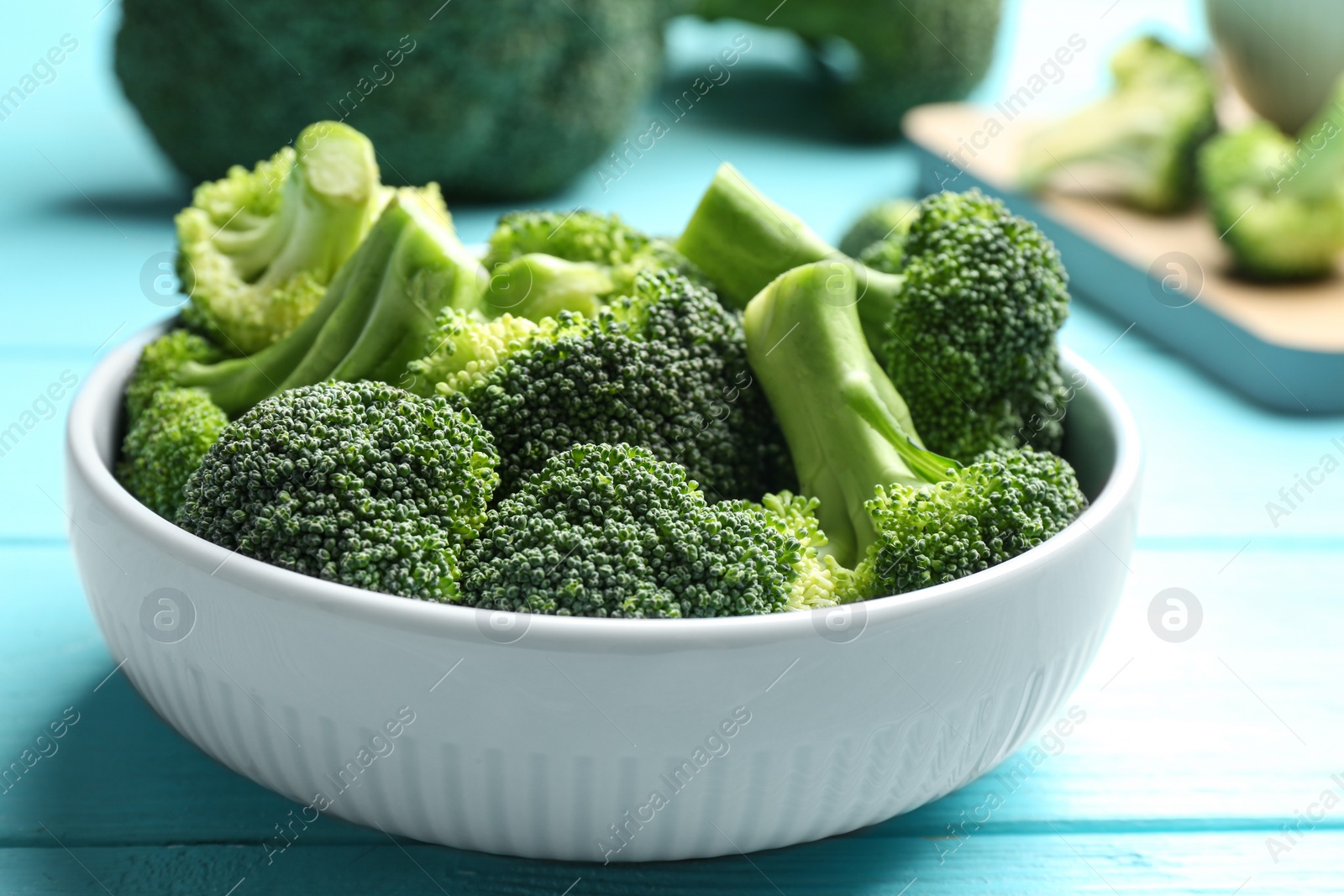 Photo of Bowl of fresh green broccoli on blue wooden table, closeup view