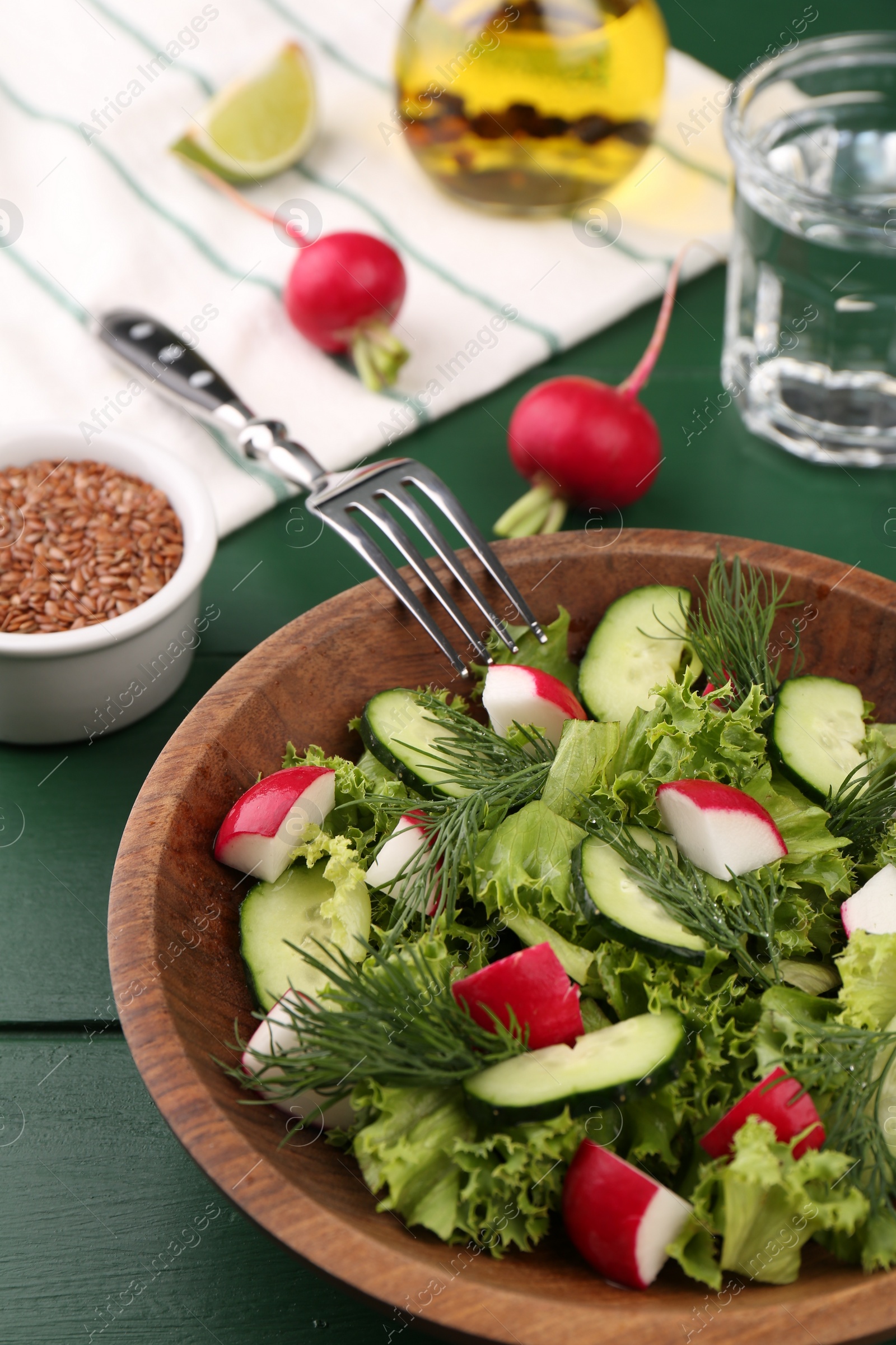 Photo of Delicious salad with radish, lettuce, dill and cucumber served on green wooden table, closeup