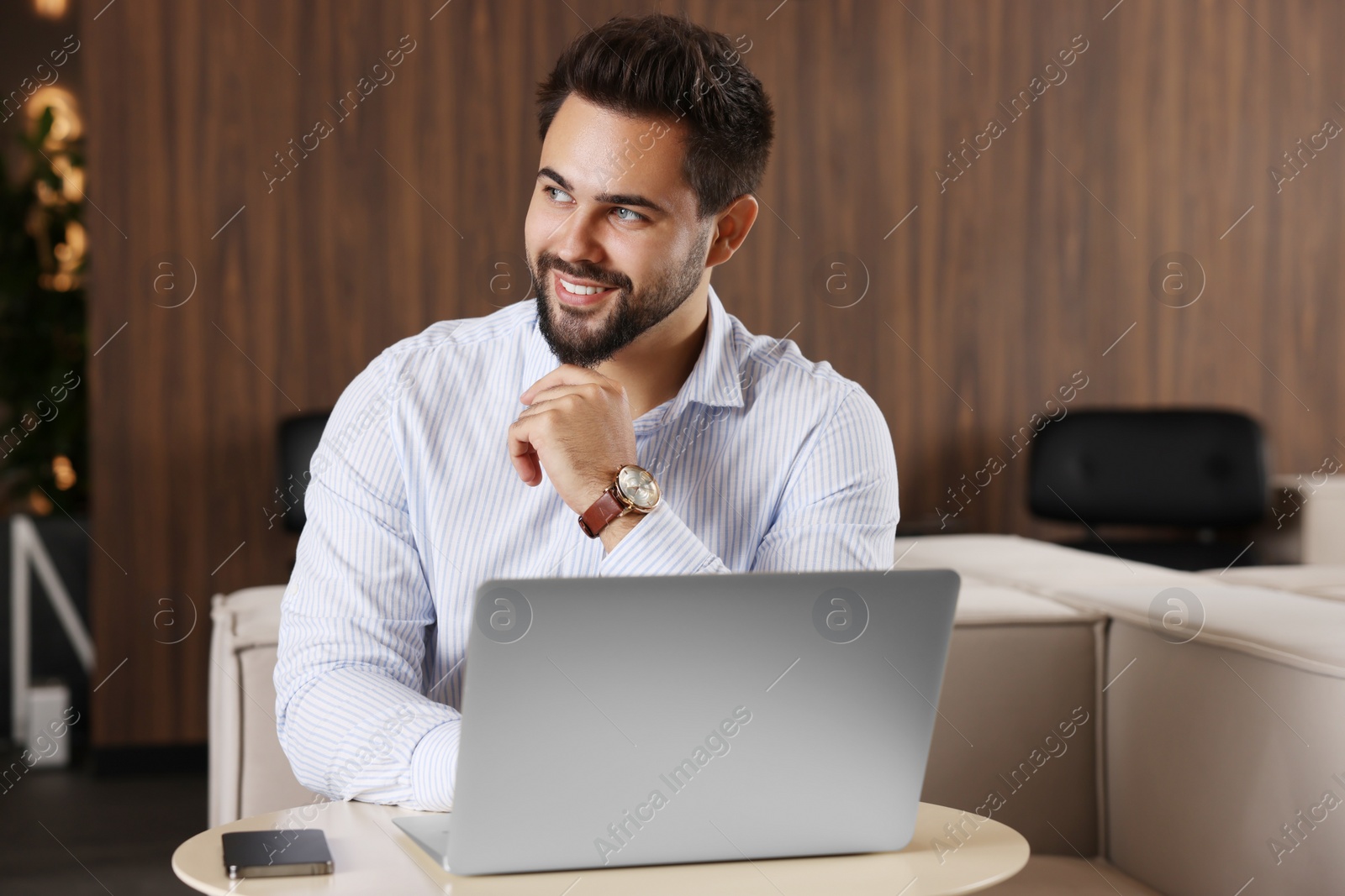 Photo of Happy young man working on laptop at table in office