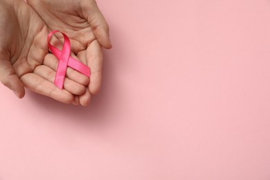 Woman holding pink ribbon on color background, top view with space for text. Breast cancer awareness concept