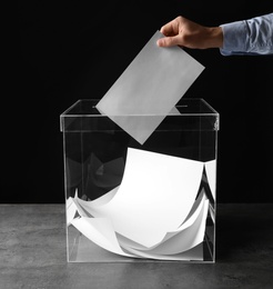 Photo of Man putting his vote into ballot box on table against black background, closeup