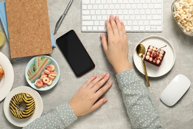 Photo of Bad eating habits. Woman working on computer at light grey table with different snacks, top view