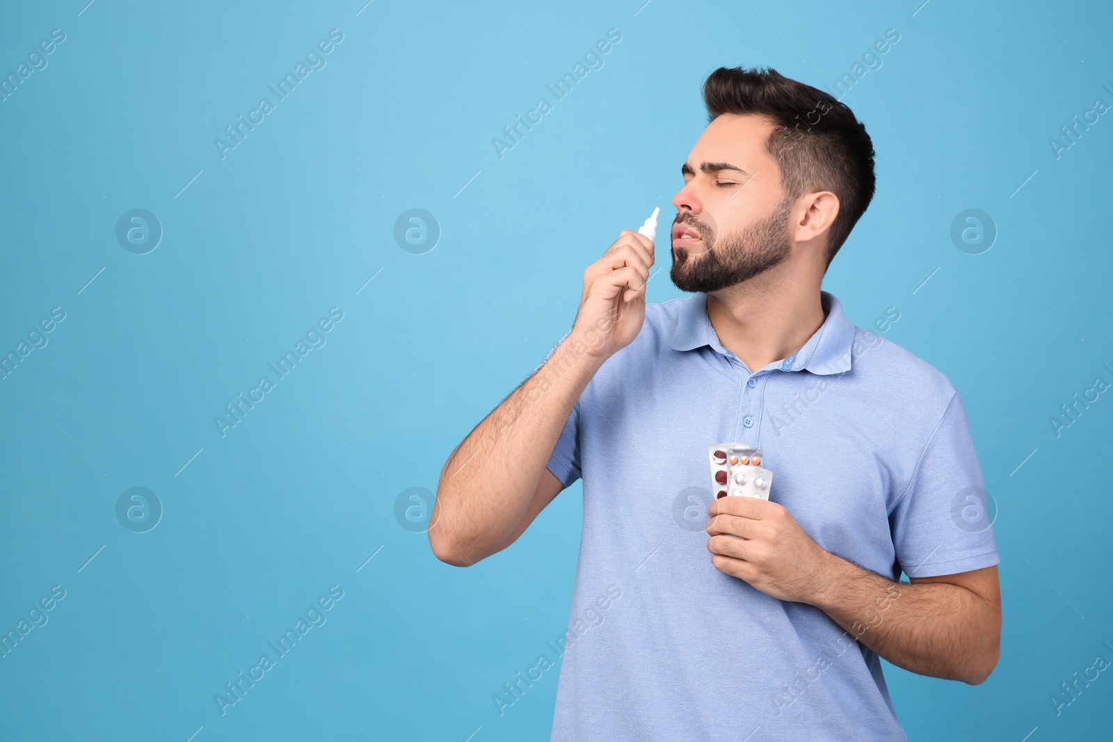 Photo of Man with pills using nasal spray on light blue background, space for text