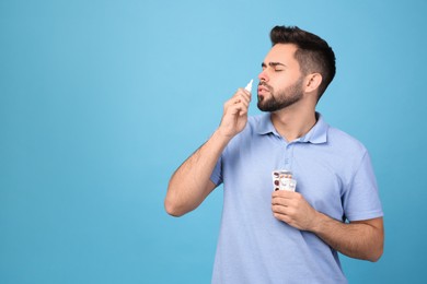 Man with pills using nasal spray on light blue background, space for text