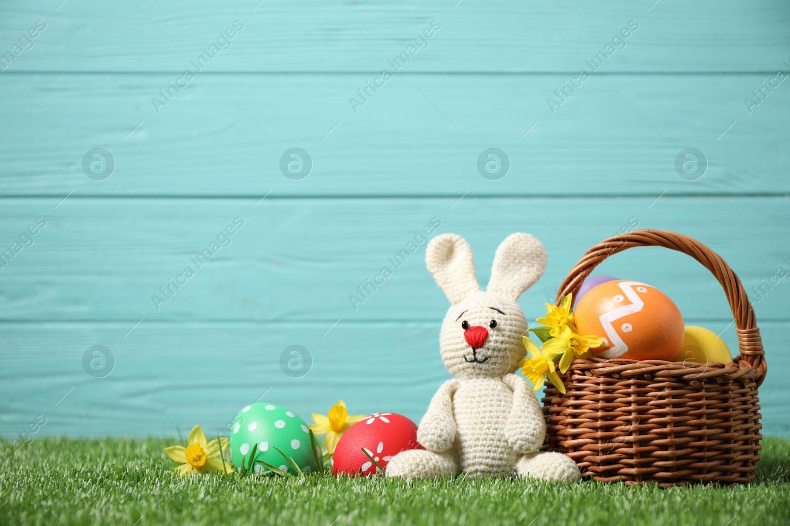 Photo of Colorful Easter eggs, basket and bunny toy on green grass against light blue wooden background