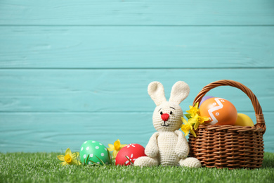 Photo of Colorful Easter eggs, basket and bunny toy on green grass against light blue wooden background