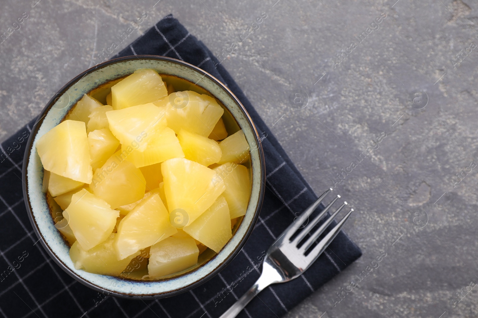 Photo of Tasty canned pineapple in bowl on grey table, flat lay. Space for text