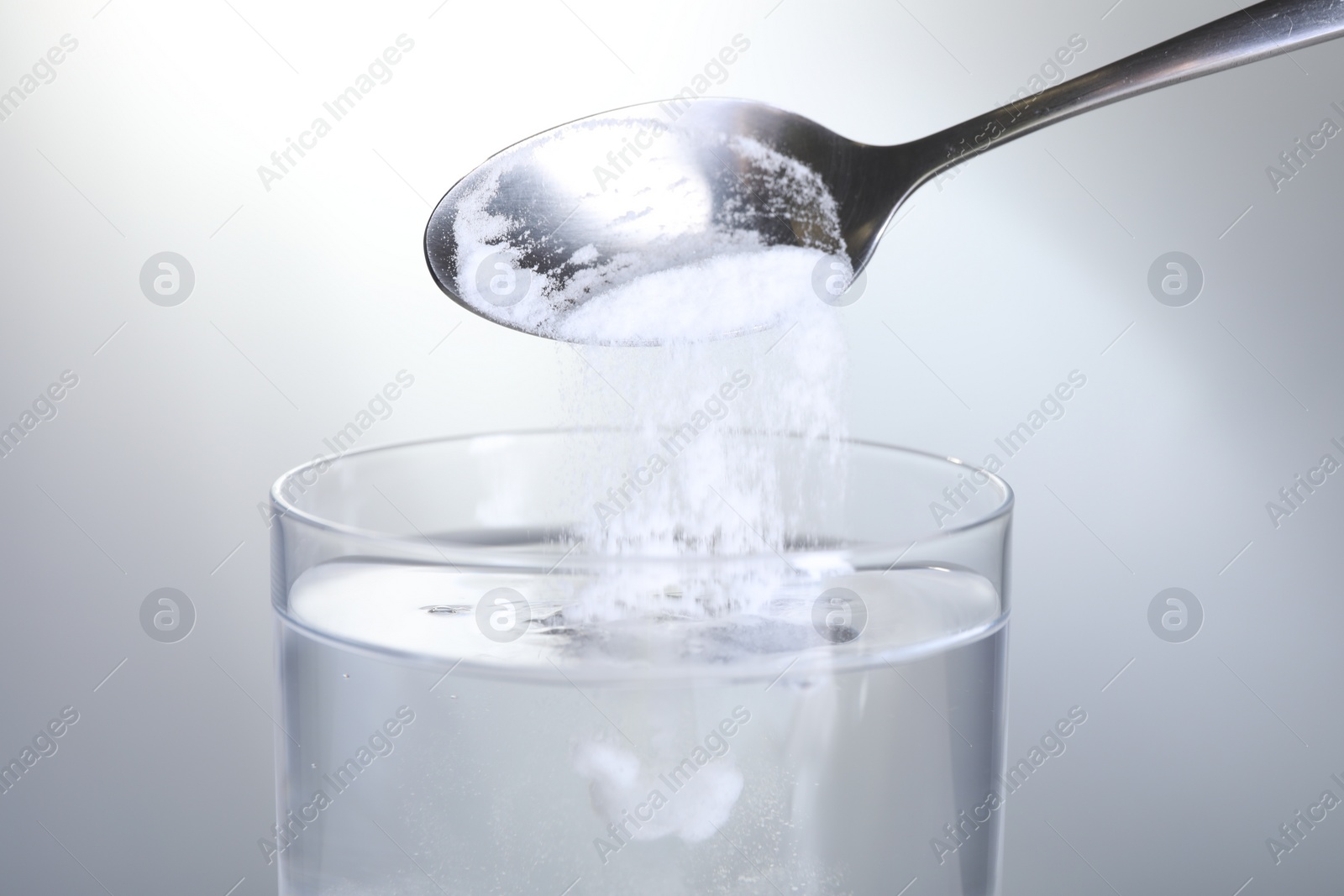 Photo of Adding baking soda into glass of water on light grey background, closeup