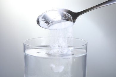 Photo of Adding baking soda into glass of water on light grey background, closeup