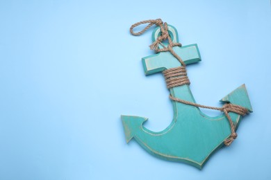 Wooden anchor with hemp rope on pale blue background, top view. Space for text