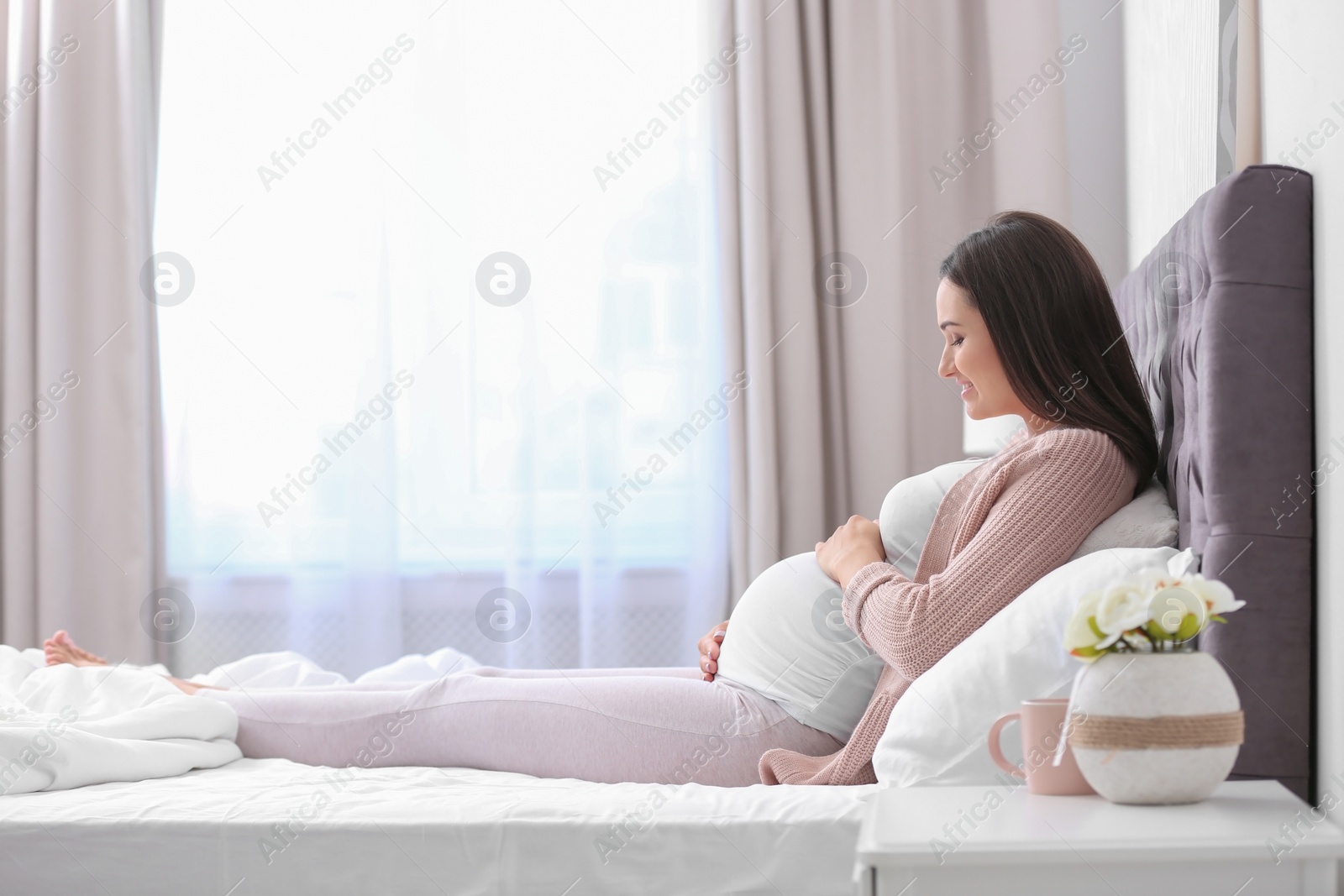 Photo of Young beautiful pregnant woman lying on bed and touching her belly at home