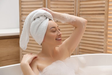 Happy woman taking bath with foam in tub indoors