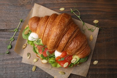 Photo of Tasty croissant with salmon, avocado, mozzarella and lettuce on wooden table, top view