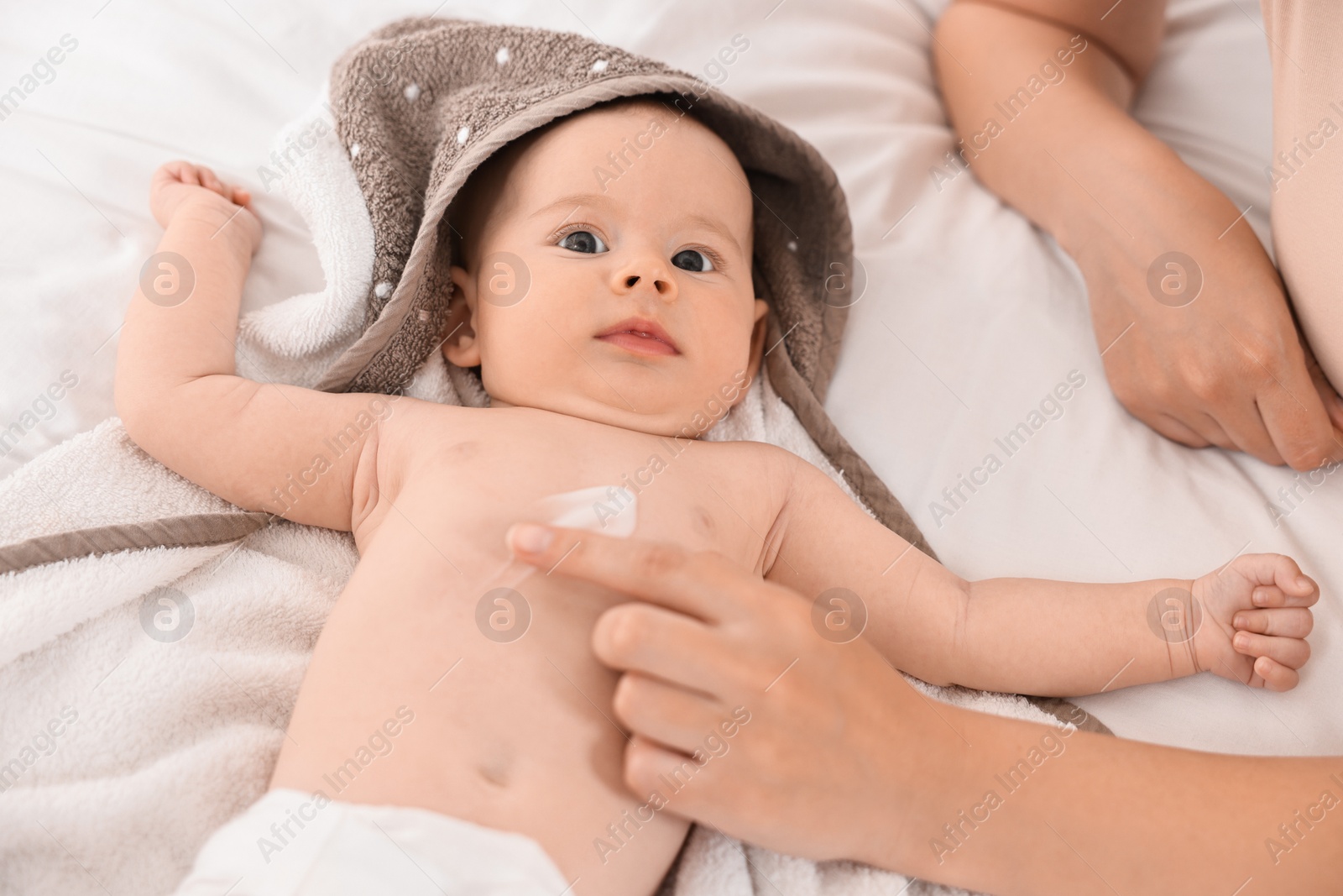 Photo of Woman applying body cream onto baby`s skin on bed, closeup