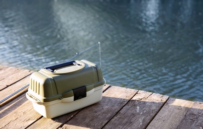 Photo of Tackle box and rod for fishing on wooden pier at riverside. Recreational activity