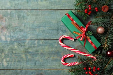 Photo of Christmas gift box, candy canes and festive decor on blue wooden table, flat lay. Space for text