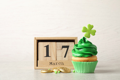 Photo of Delicious decorated cupcake, wooden block calendar and coins on light table. St. Patrick's Day celebration