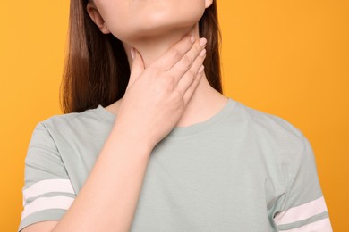Photo of Woman with sore throat on orange background, closeup