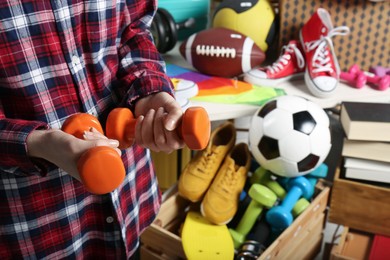Photo of Woman holding dumbbells near many different stuff indoors, closeup. Garage sale