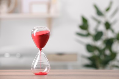 Photo of Hourglass with red flowing sand on table against blurred background. Space for text