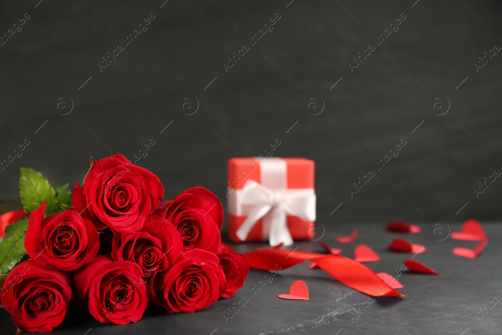 Photo of Beautiful red roses, paper hearts and gift box on dark table, space for text. St. Valentine's day celebration