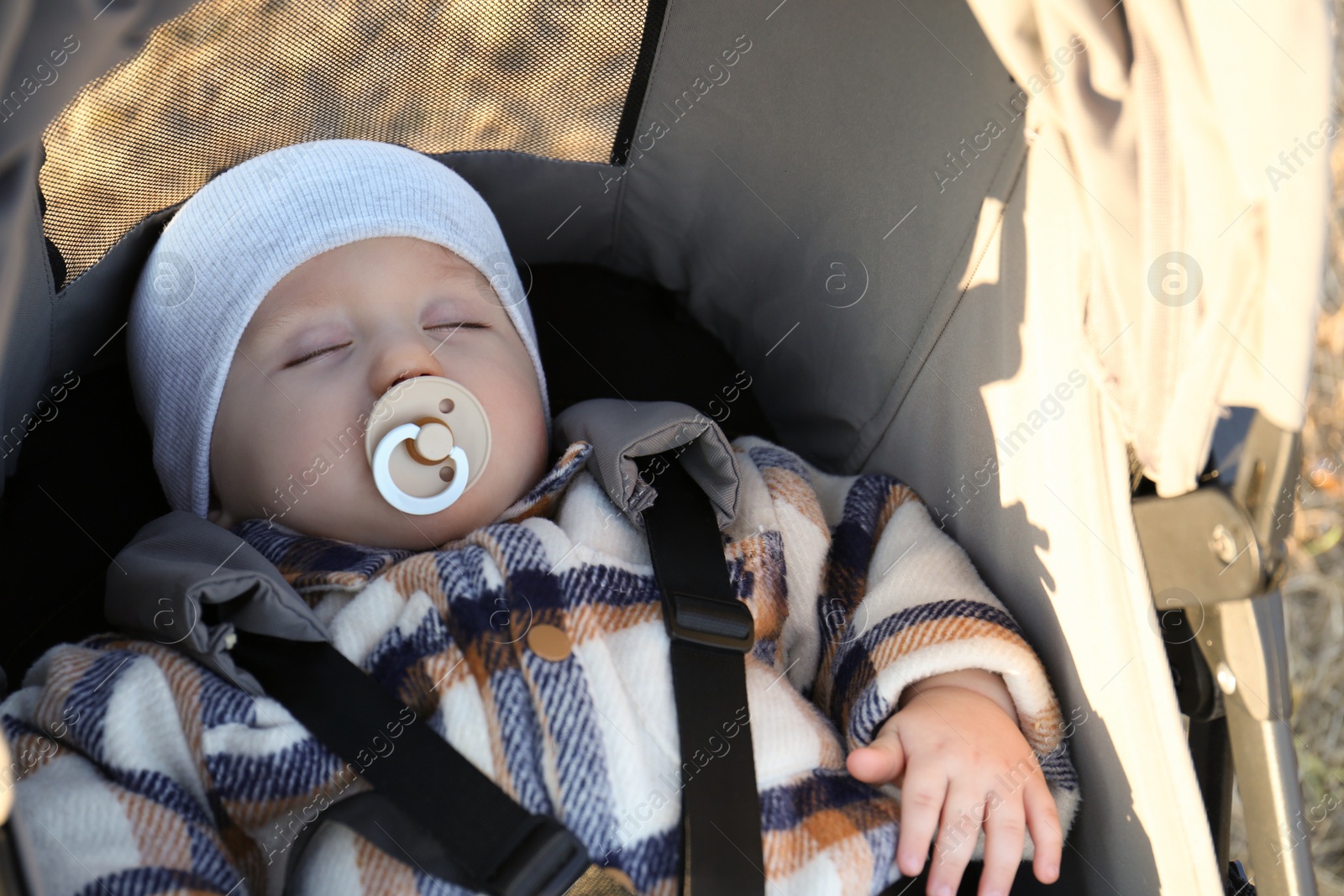 Photo of Cute little child with pacifier sleeping in stroller outdoors