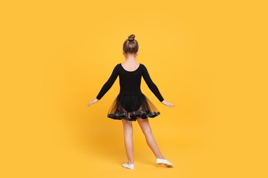 Photo of Cute little girl in black dress dancing on yellow background, back view