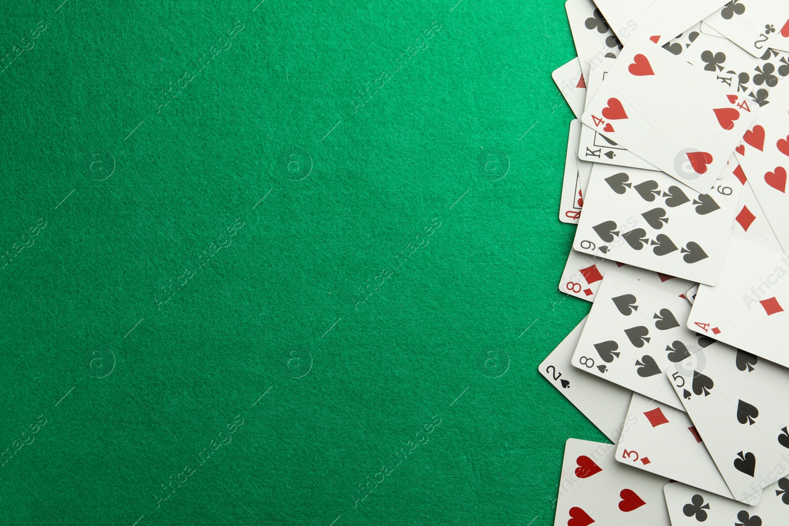 Photo of Scattered playing cards on green table, top view. Space for text