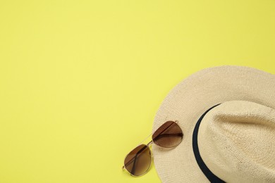 Hat and sunglasses on yellow background, flat lay with space for text. Sun protection