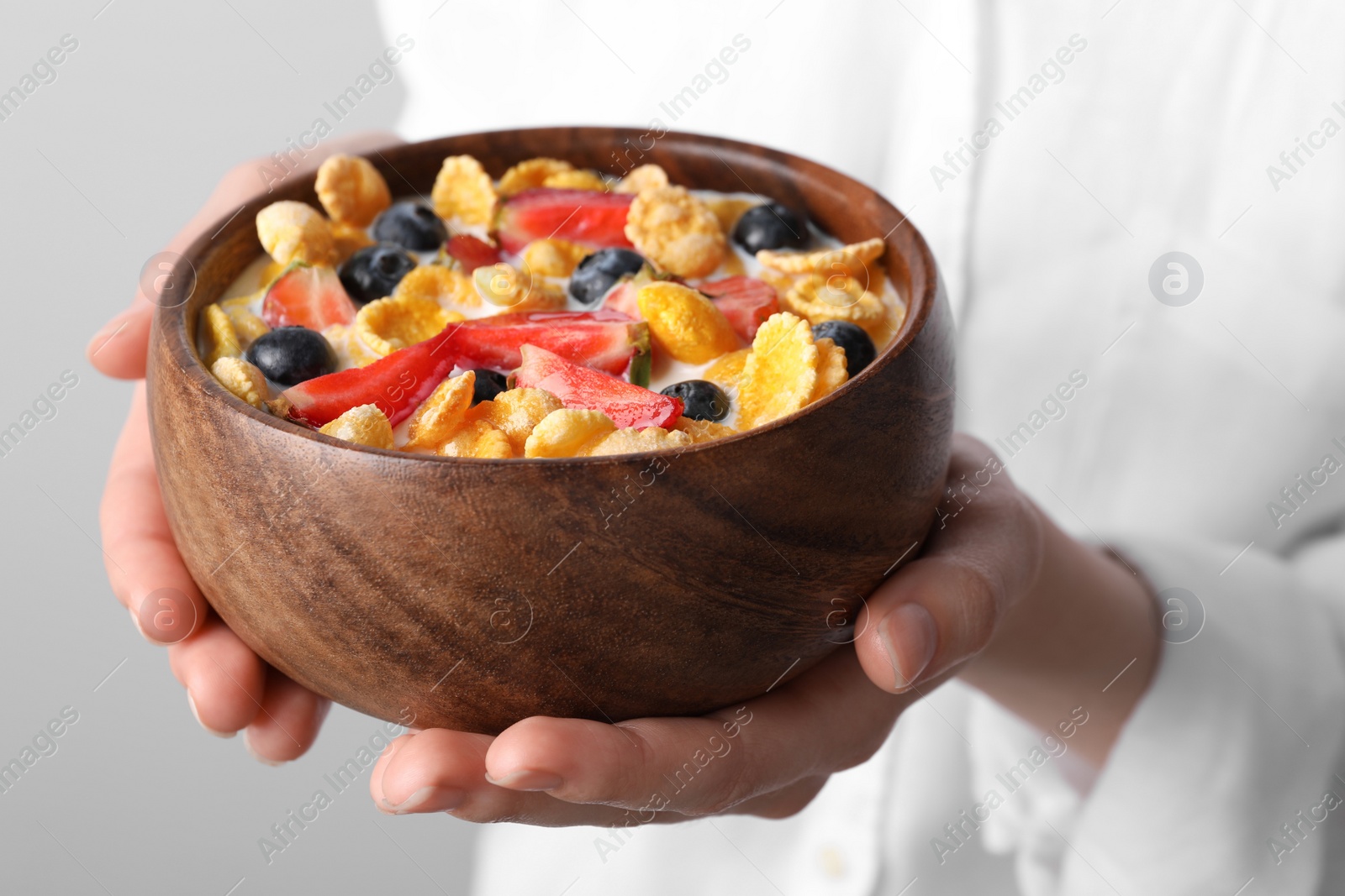 Photo of Woman holding bowl of crispy corn flakes with milk and berries, closeup