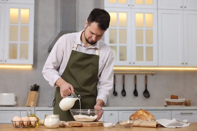 Photo of Making bread. Man pouring milk into bowl with flour at wooden table in kitchen, space for text